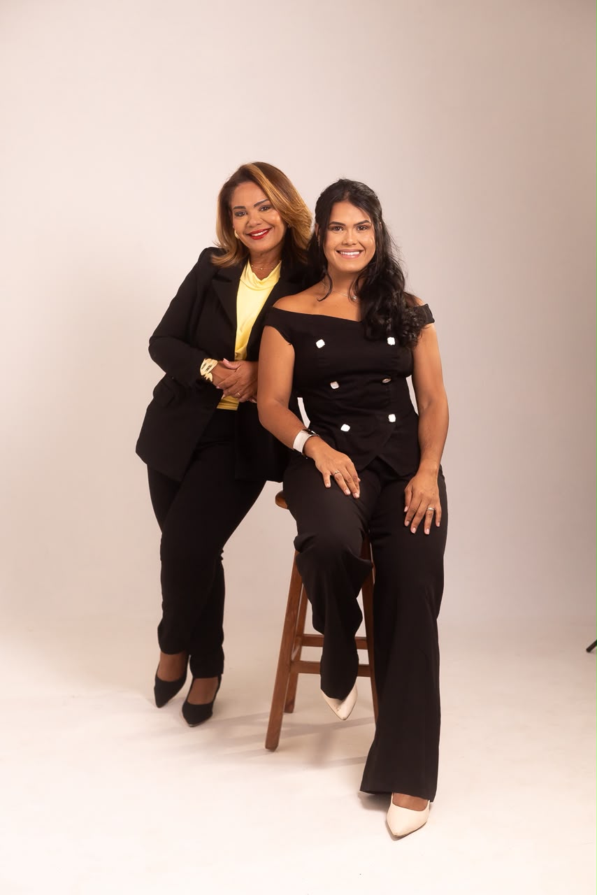 Duas mulheres sorrindo juntas, com roupas pretas, em um retrato de estúdio